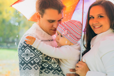 A family with a young child, faces obscured for privacy, sharing a tender moment under colorful umbrellas, symbolizing the protection offered by critical care illness insurance.