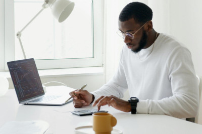 A person sitting at a desk working on a laptop with documents and a coffee mug, representing state disability inclusion in the workplace.