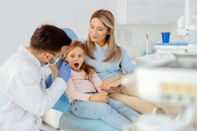 A dental professional examines a young patient’s teeth while an adult stands by, highlighting FEDVIP benefits.